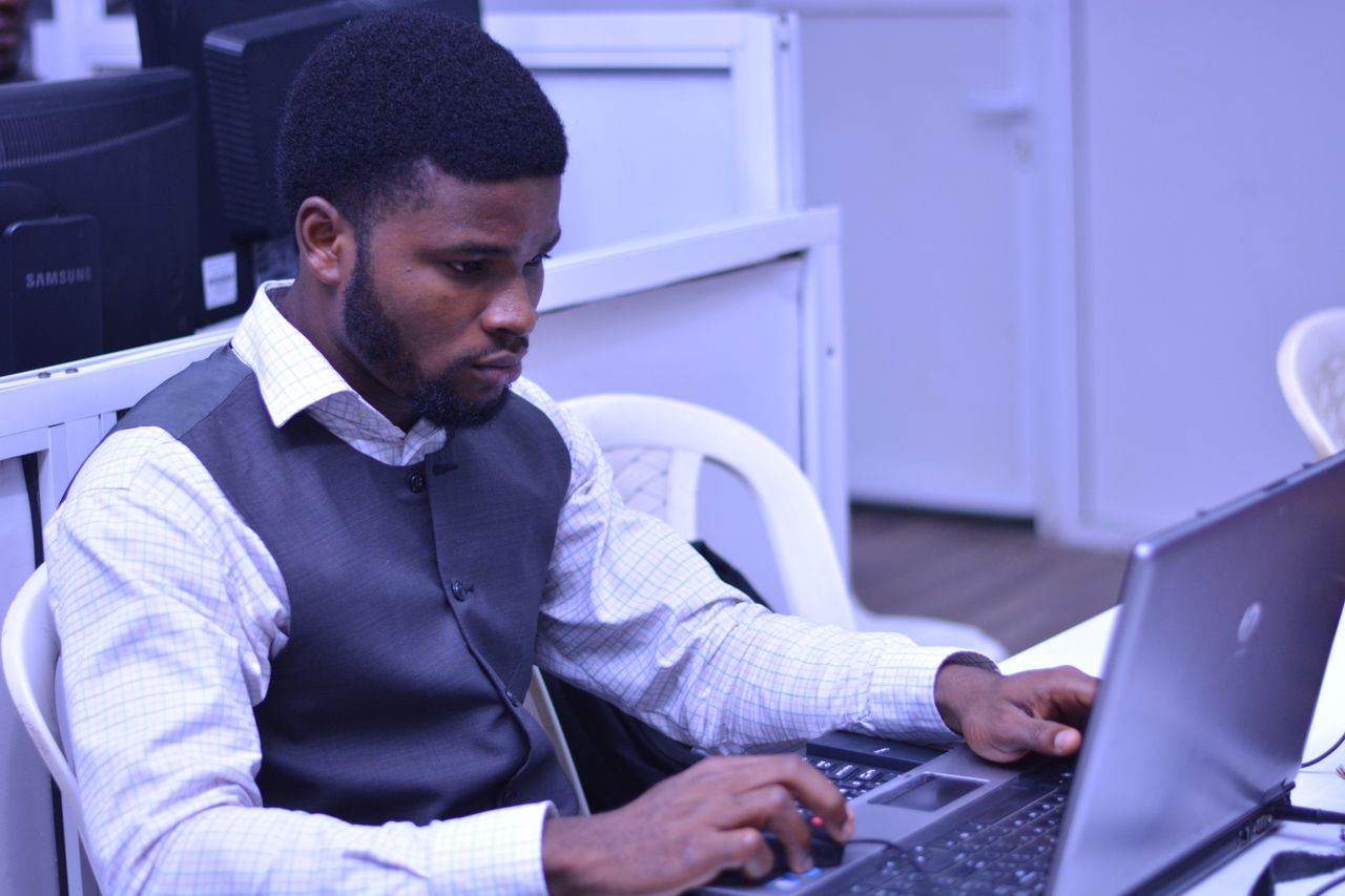 Young man with a beard intensely working on a laptop in a modern office environment.